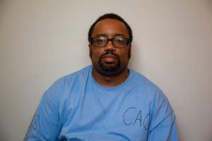 Man with glasses and blue t-shirt against a blank background.