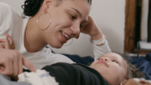 Woman playing with a young toddler on a bed.